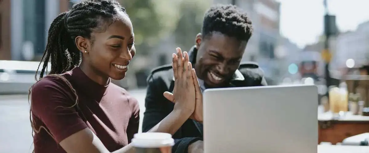 Two students giving high five while working on laptop outside