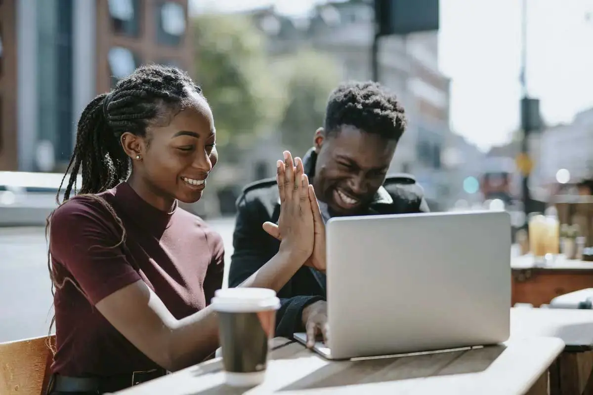 Two students giving high five while working on laptop outside