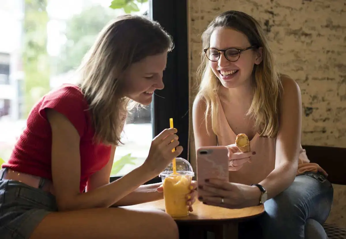 Two students looking at phone while enjoy a snack