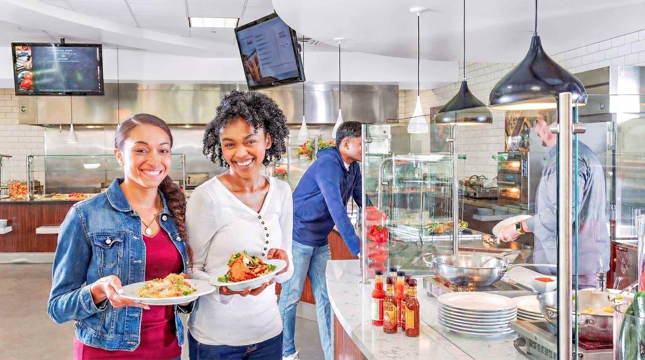 Two students happily holding plates of food in the middle of serving area